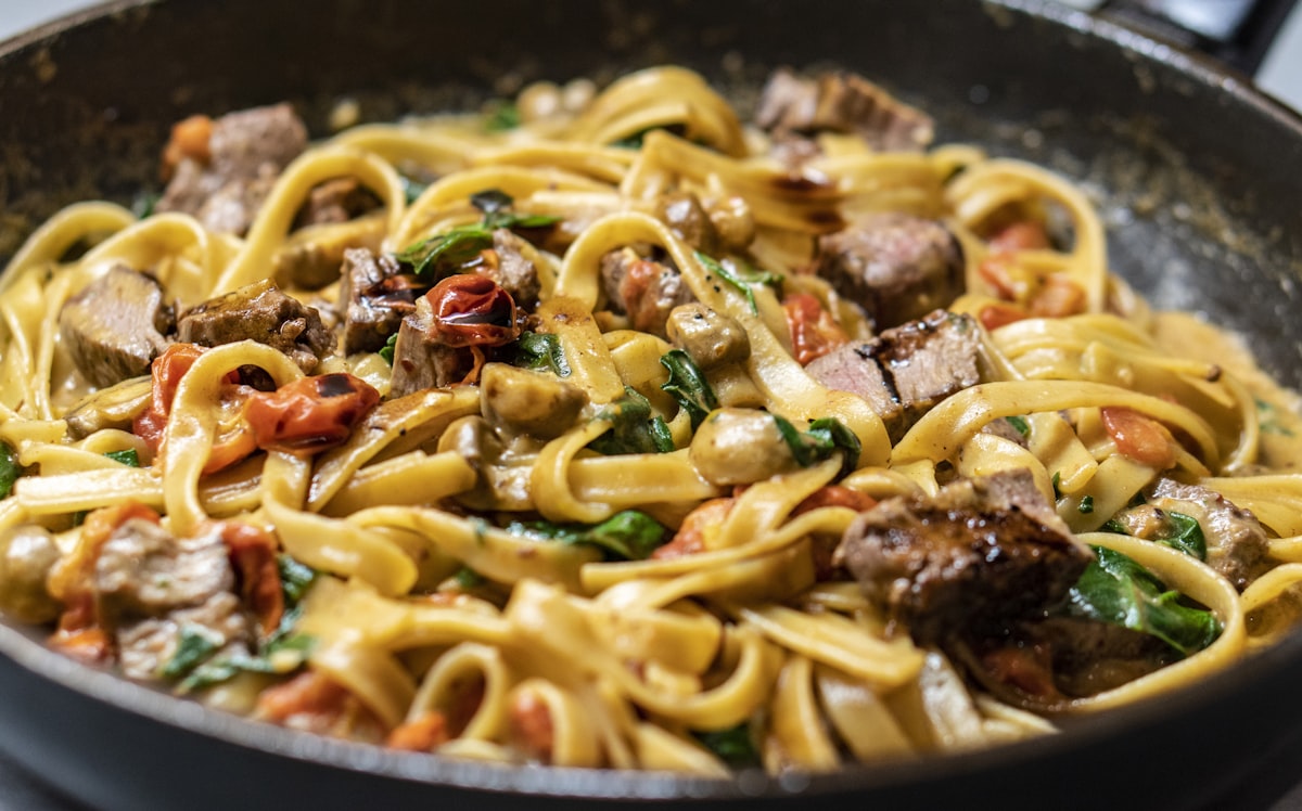 フライパンの中で牛肉のラグーと絡める手打ちフェットチーネ。厨房の躍動感ある調理シーン